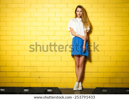 Full Length Portrait of Trendy Hipster Girl Standing at the Yellow Brick Wall Background. Urban Fashion Concept. Copy Space.