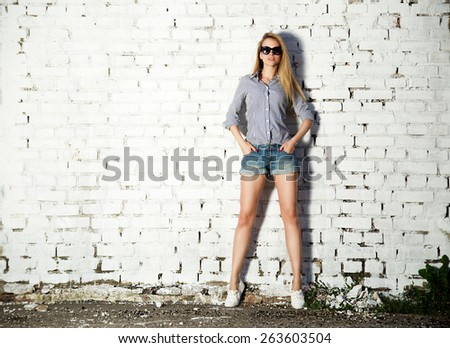 Full Length Portrait of Trendy Hipster Girl with Hands in Pockets on White Brick Wall Background. Trendy Urban Fashion Concept. Copy Space.