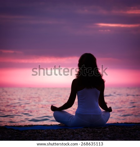 Silhouette of Woman Meditating in Lotus Position by the Sea at Sunset. Rear View. Nature Meditaion Concept. Toned Instagram Styled Photo.