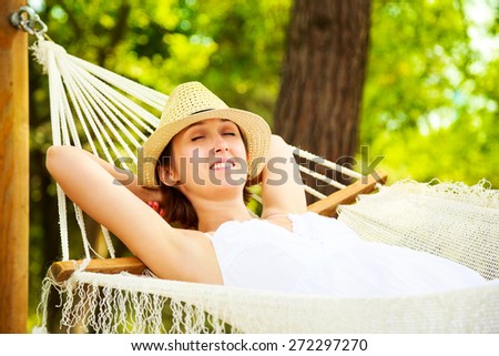 Happy Young Woman Relaxing in a Hammock and Smiling. Hands Behind Head. Summer Nature Daydreaming Concept.