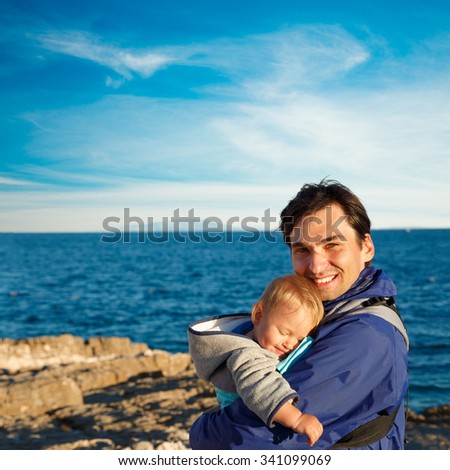 Happy Father with His Little Son in Carrier on Sea Background. Family Recreation Concept. Square Photo with Copy Space.