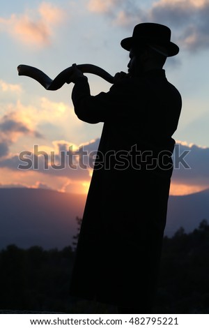 orthodox Jew blowing the shofar of Rosh Hashanah.\
indistinct man in background blur blows a long yemenite shofar horn with focus on the open end of the horn; isolation on forest.