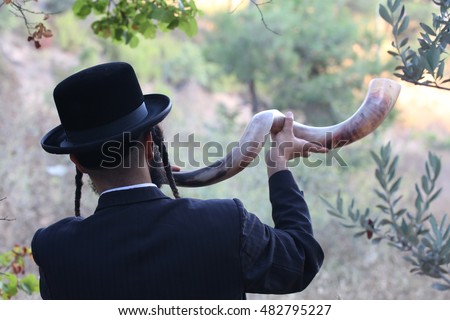 orthodox Jew blowing the shofar of Rosh Hashanah.
indistinct man in background blur blows a long yemenite shofar horn with focus on the open end of the horn; isolation on forest.