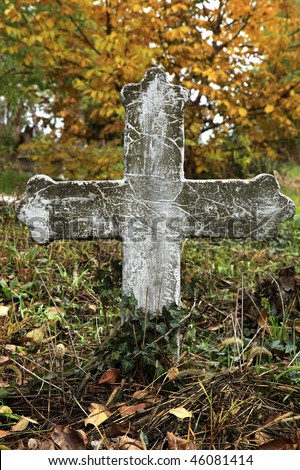 Stone cross in a cemetery with colorful tree in the background in autumn