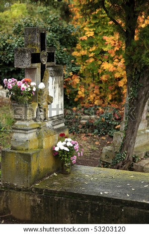 Cross with colorful flowers in a cemetery in autumn