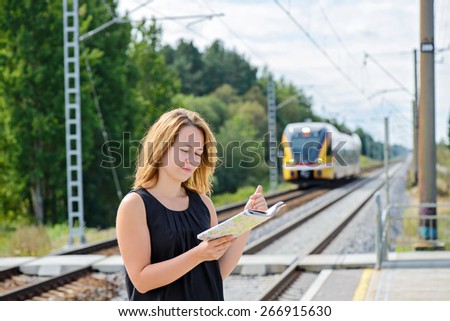 Female looking to the map on the platform of railway station. Train is coming.