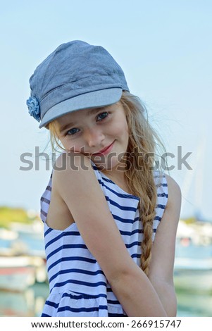 Portrait of beautiful little girl in denim cap and striped clothes posing outdoors