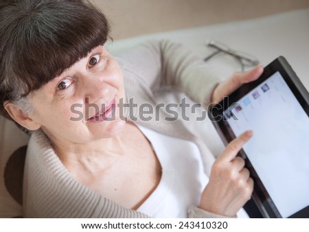 Pension age good looking woman looking internet in tablet device. View from the top