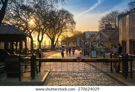 LONDON, UK - APRIL 15, 2015: Tower park in sunset. River Thames side walk with people resting by the water