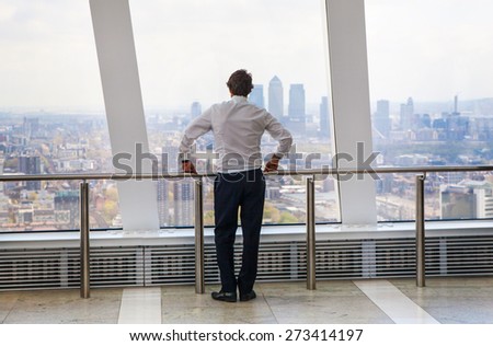 LONDON, UK - APRIL 22, 2015: Businessman looking at London through the window of Walkie-Talkie building. View includes Canary Wharf business and banking aria. Business concept image