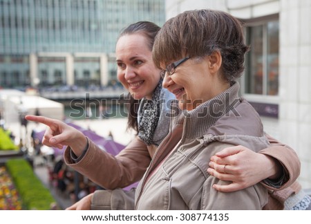Outdoor family portrait of pension age Mother and her daughter in the city, smiling and looking around. Two generation, happiness and care  concept