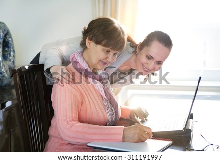 Younger woman helping an elderly person using laptop computer for internet search. Young and pension age generations working together.
