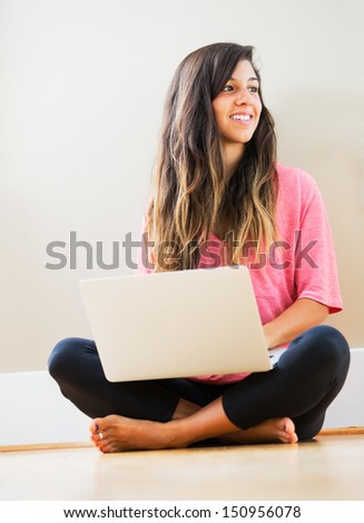 Portrait of beautiful happy young woman sitting on floor with a laptop smiling - Indoor