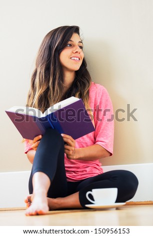 Portrait of beautiful happy young woman sitting on floor reading a book smiling - Indoor