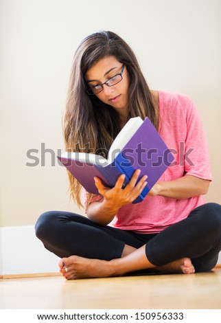 Portrait of beautiful happy young woman sitting on floor reading a book smiling - Indoor