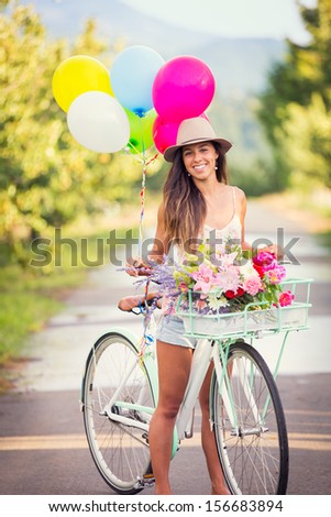 Beautiful young woman on bike in park with balloons