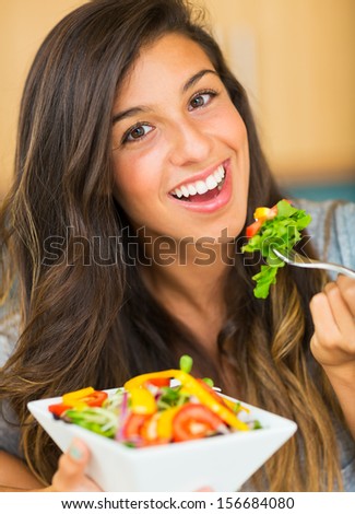 Portrait of beautiful young woman eating a bowl of healthy organic salad and smiling