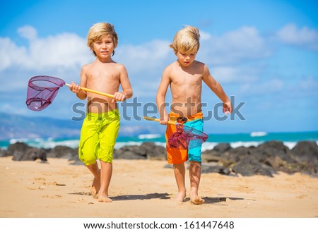 Two young boys having fun on tropical beach, happy best friends playing with fishing nets, friendship concept