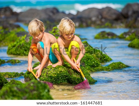 Two young boys having fun on tropical beach, happy best friends playing with fishing nets, friendship concept
