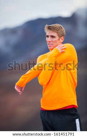 Young attractive athletic man, wearing sporty cloths on trail, stretching before run