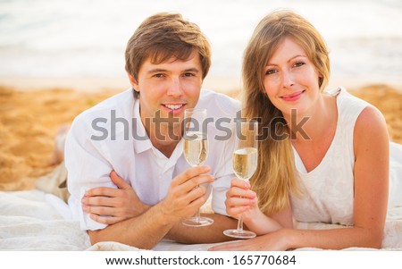 Honeymoon concept, Man and Woman in love, Couple enjoying glass of champagne on tropical beach at sunset