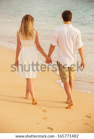 Young couple in love, Attractive man and woman enjoying romantic walk on the beach at sunset holding hands