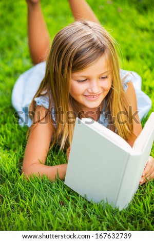 Cute little girl reading book outside on grass, relaxing outside in backyard