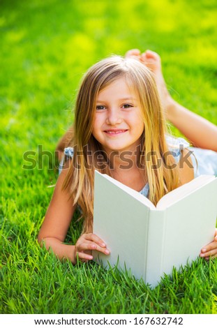 Cute little girl reading book outside on grass, relaxing outside in backyard