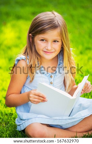 Cute little girl reading book outside on grass in backyard