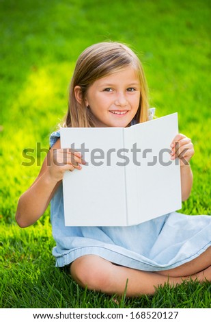 Adorable cute little girl reading book in the garden, outside on grass