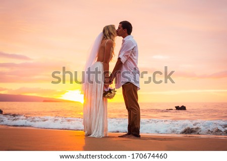 Married couple, bride and groom, kissing at sunset on beautiful tropical beach in Hawaii