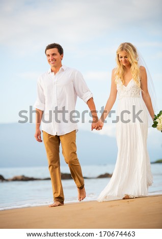 Married couple, bride and groom holding hands at sunset on beautiful tropical beach in Hawaii