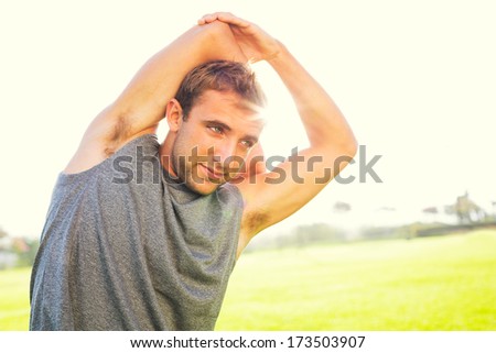 Attractive fit young man stretching before exercise workout, sunrise early morning backlit. Healthy lifestyle sports fitness concept.