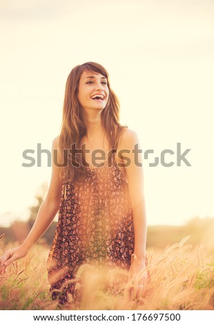 Beautiful young woman outdoors. Romantic Model in Sun Dress in Golden Field at Sunset. Happy Emotions, Laughing. Backlit. Warm color tones