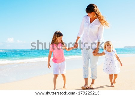 Mother and two adorable young daughters walking along on the beach
