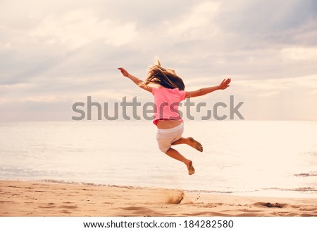 Happy Young Girl Jumping For Joy on the Beach at Sunset
