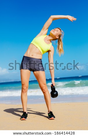 Young attractive woman doing kettle bell exercises outside. Fitness woman working out at the beach. Fitness Concept.