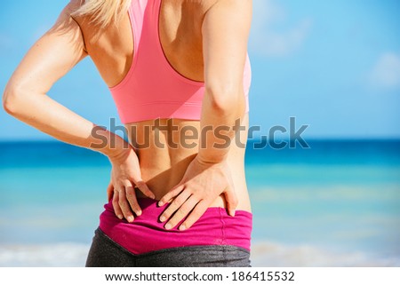 Back Pain. Athletic fitness woman rubbing the muscles of her lower back. Sports exercising injury.
