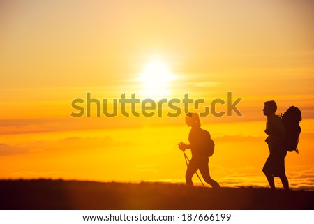 Silhouettes of two hikers with backpacks walking at sunset. Trekking and enjoying the sunset view from mountain top above the clouds.