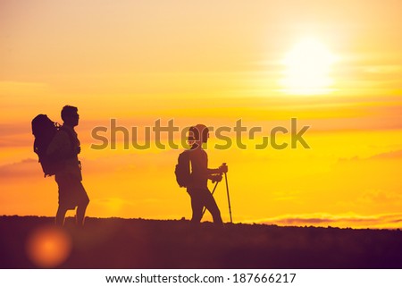 Silhouettes of two hikers with backpacks walking at sunset. Trekking and enjoying the sunset view from mountain top above the clouds.