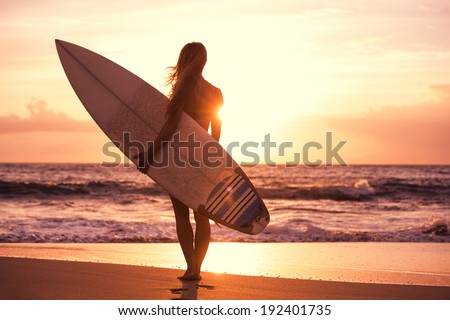 Silhouette of beautiful surfer girl on the beach at sunset