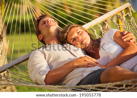 Romantic couple relaxing in tropical hammock at sunset