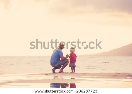 Father and son holding hands walking on the beach at sunset