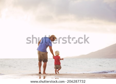 Father and son holding hands walking on the beach at sunset