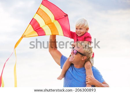 Happy father and son playing with kite at the beach at sunset