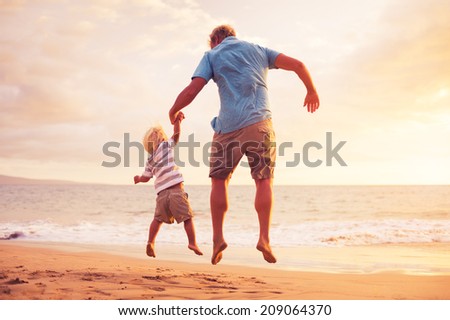 Father and son jumping for joy on the beach at sunset
