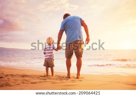 Father and son standing on the sea shore holding hands at sunset