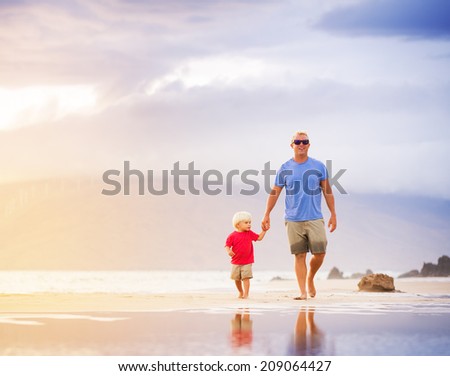 Happy father and son walking on the beach at sunset holding hands