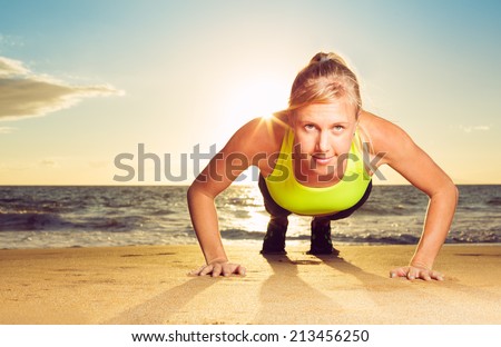 Fitness young woman doing push ups on beach at sunset. Outdoor workout.