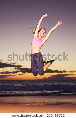 Attractive young happy fitness woman jumping on the beach at sunset